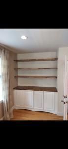 Built-in corner shelves above white cabinets in a small room with hardwood floor and ceiling light