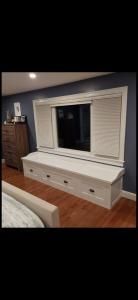 Bedroom with white shutters over a large window and a white storage bench beneath it on hardwood floor