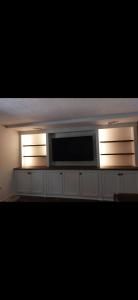 Living room media wall with a central TV, lit side shelves, and white cabinets below