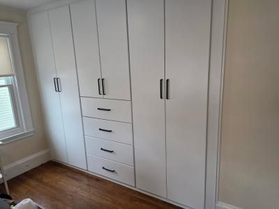White built-in wardrobe with central drawers in a bright room with wood flooring and a window.