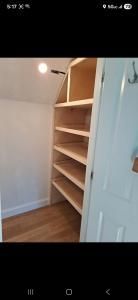 Open closet with built-in wooden shelves and a hanging rod next to a white door in a room with wood flooring