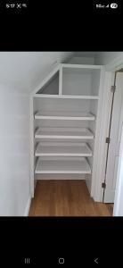 Empty white closet with built-in shelves and wood floor under a slanted ceiling