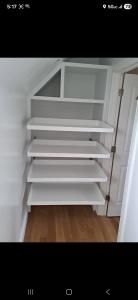White built-in storage shelves in a small closet or under-stairs nook with a wooden floor.