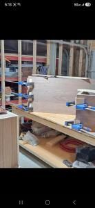 Clamps holding a plywood panel on a workbench in a workshop, with tools and shelving in the background