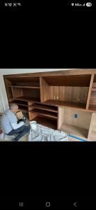Person assembling a large wooden shelving unit in a room, with tools and packing materials on the floor