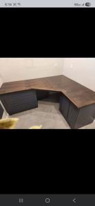 Dark L-shaped wooden desk with black drawers against a beige wall in a corner room