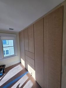 Built-in wood-paneled storage wall in a bright room with a window and sunlight on the floor