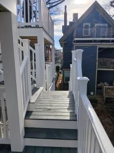 Narrow white wooden deck walkway between houses, with railings and steps leading to a porch.