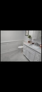 Bright white bathroom with a vanity, round mirror, and toilet beside a tiled wall.