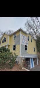Yellow three-story house with white trim and a gray roof on a wooded hillside