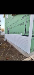Exterior wall of a building under construction, wrapped in green house wrap with white siding below.