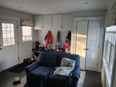 Small room with navy couch, coat rack, white cabinets, and bright windows on the right.