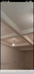 Interior ceiling with white beams and paneling, lit by a single hanging bulb.
