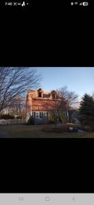 Brick house with a red roof and bare trees in front, lit by warm sunlight.