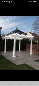 White gazebo with a dark roof and columns on a brick patio in a backyard