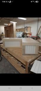 Workshop table with two unfinished wooden cabinet panels in a cluttered woodworking shop.