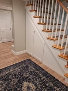 Hallway with staircase, white railings, wood steps, and patterned rug in a light-colored home