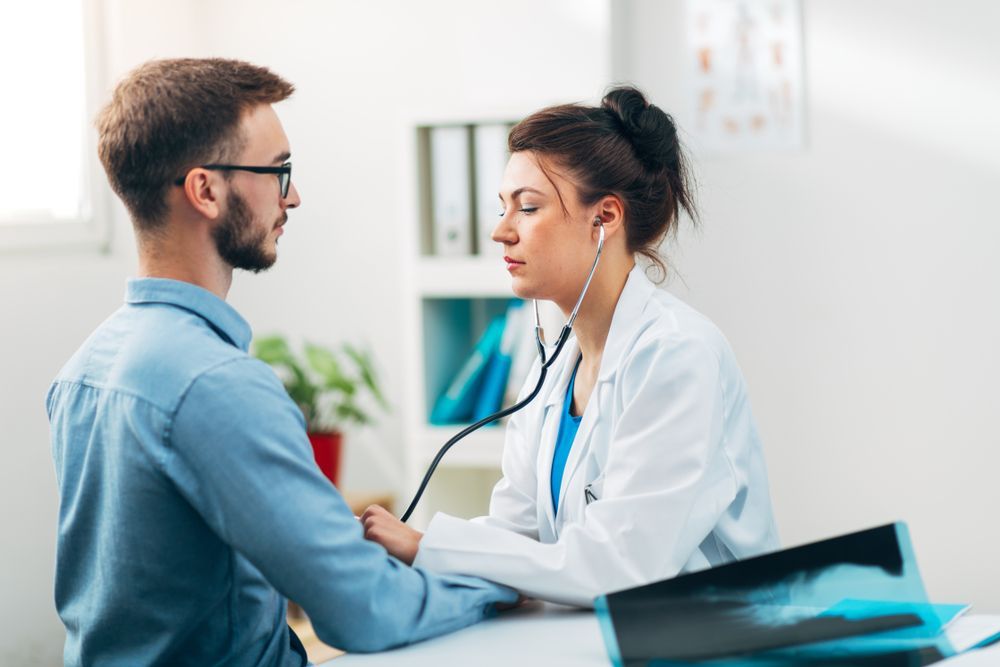 Doctor Checking a Seated Patient With a Stethoscope in a Bright Clinic Office — HealthHub Taree in Taree, NSW