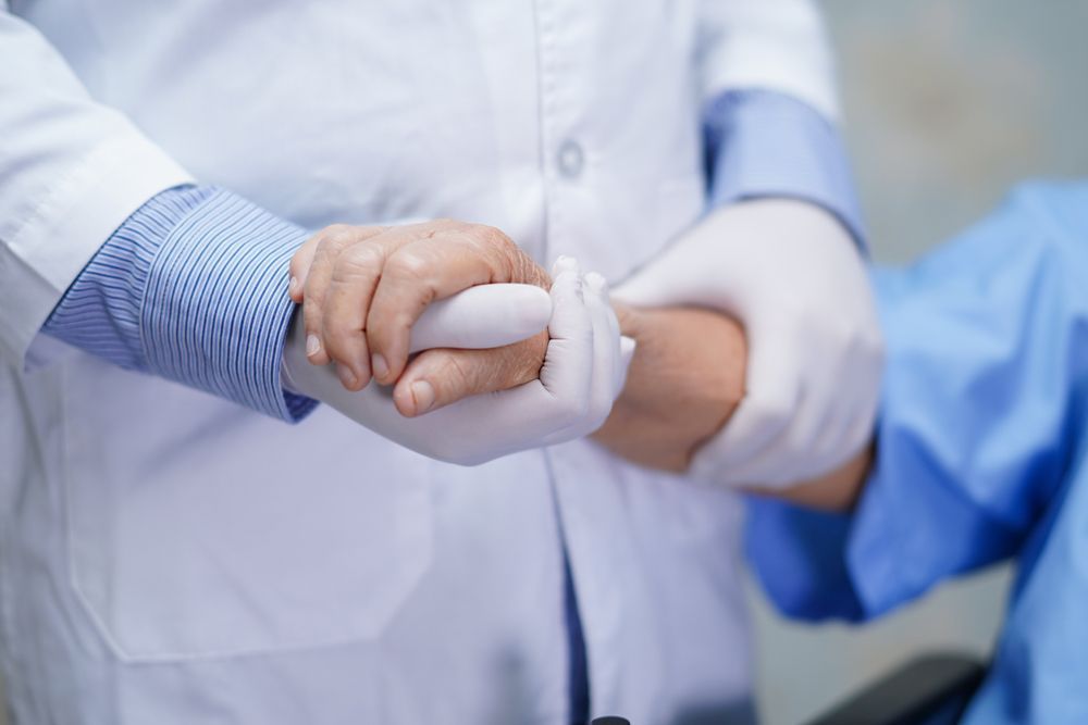 Two People Clasping Hands in a Supportive Gesture, Wearing White Medical Coats and Gloves — HealthHub Taree in Taree, NSW