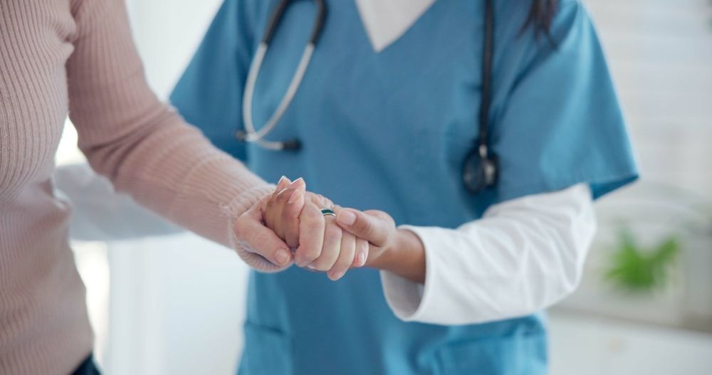 Nurse in Blue Scrubs Holding a Patient’s Hand in a Clinical Setting — HealthHub Taree in Taree, NSW