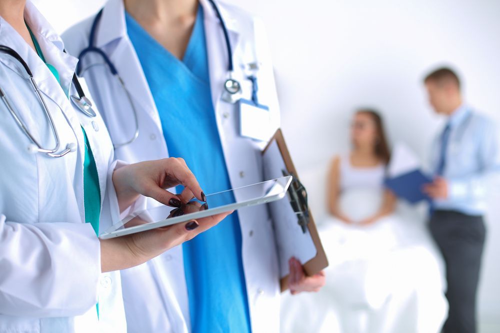 Doctors in White Coats Reviewing a Clipboard in a Bright Hospital Hallway — HealthHub Taree in Taree, NSW