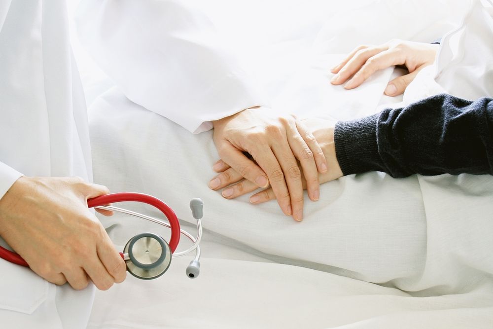 Hands Comforting a Patient in a Hospital Bed While a Doctor Holds a Stethoscope — HealthHub Taree in Taree, NSW