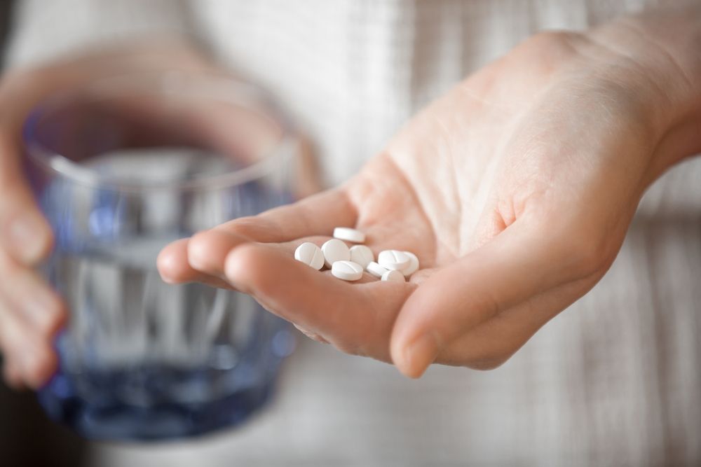 Hand Holding Several White Pills Beside a Glass of Water — HealthHub Taree in Taree, NSW