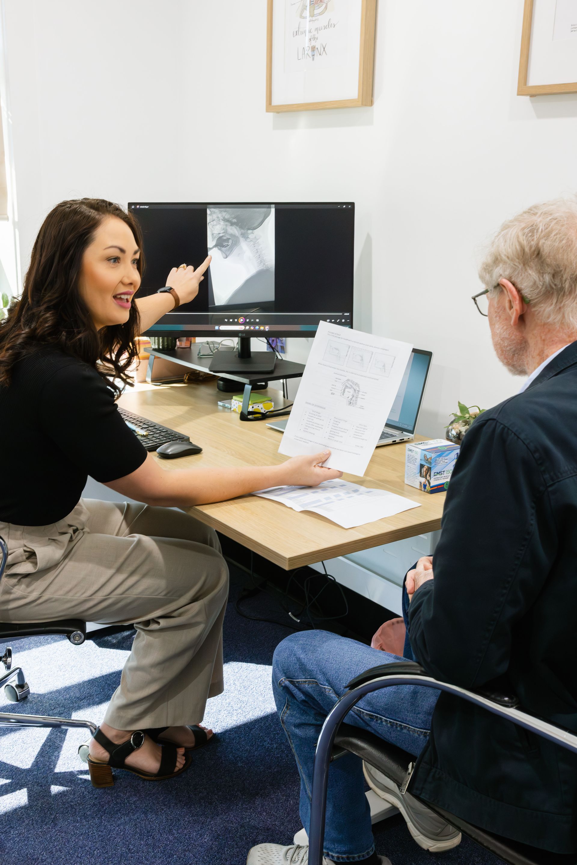 Two People Discussing a Paper at A Desk with A Computer in An Office — HealthHub Taree in Taree, NSW