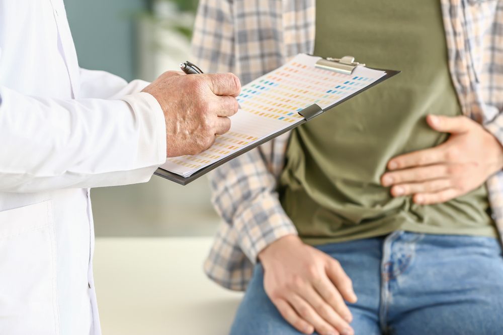 Doctor Taking Notes on a Clipboard Beside a Patient Holding Their Abdomen — HealthHub Taree in Taree, NSW