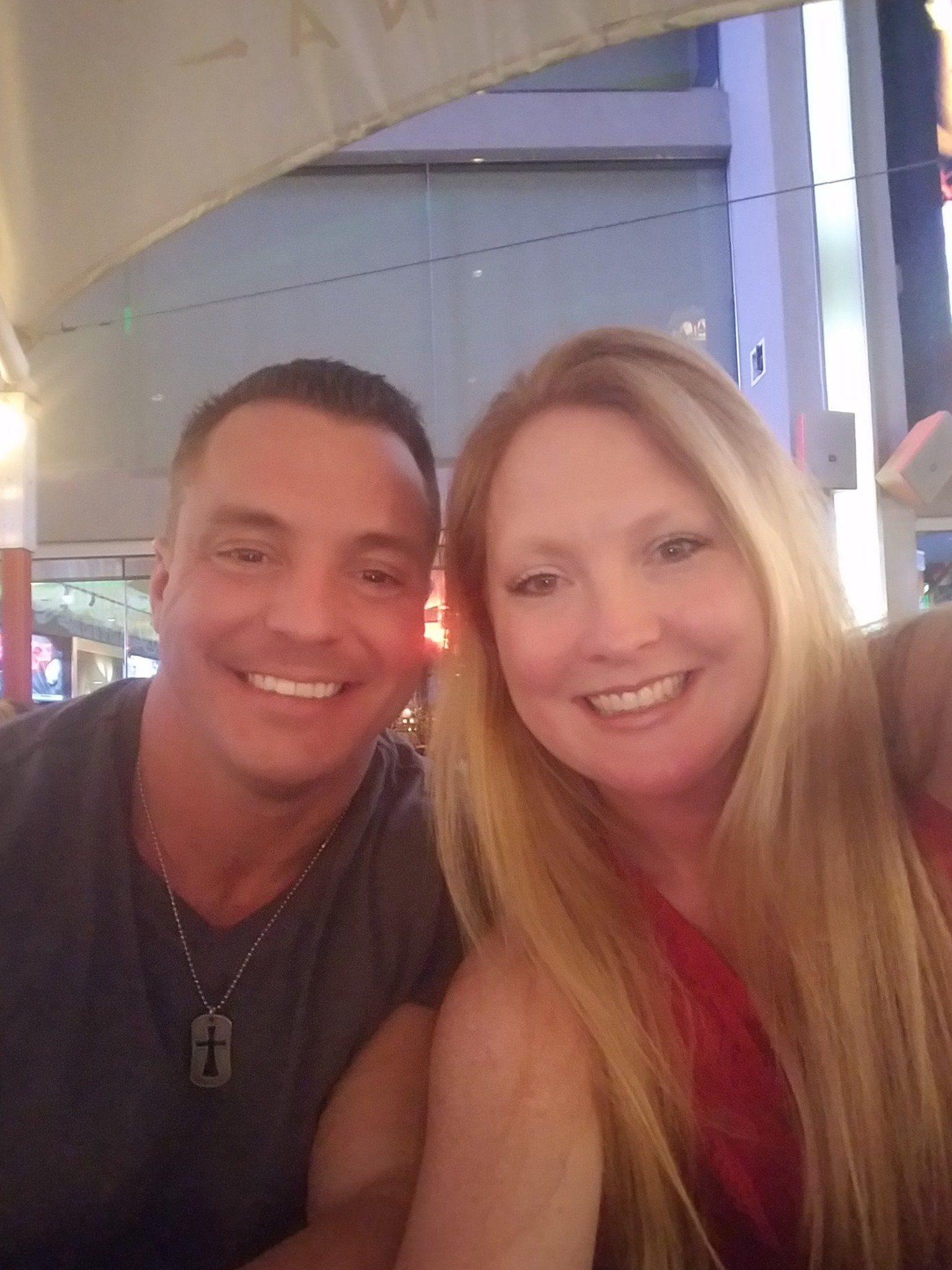 Smiling couple seated outdoors, man in grey shirt, woman in red, warm lighting.