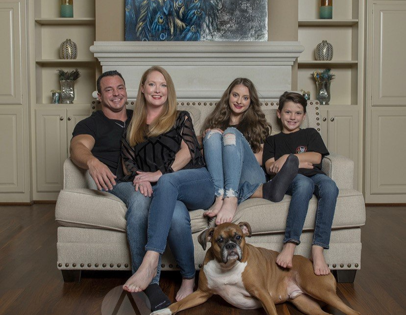 Family of four and a dog sitting on a couch in a living room, smiling at the camera.