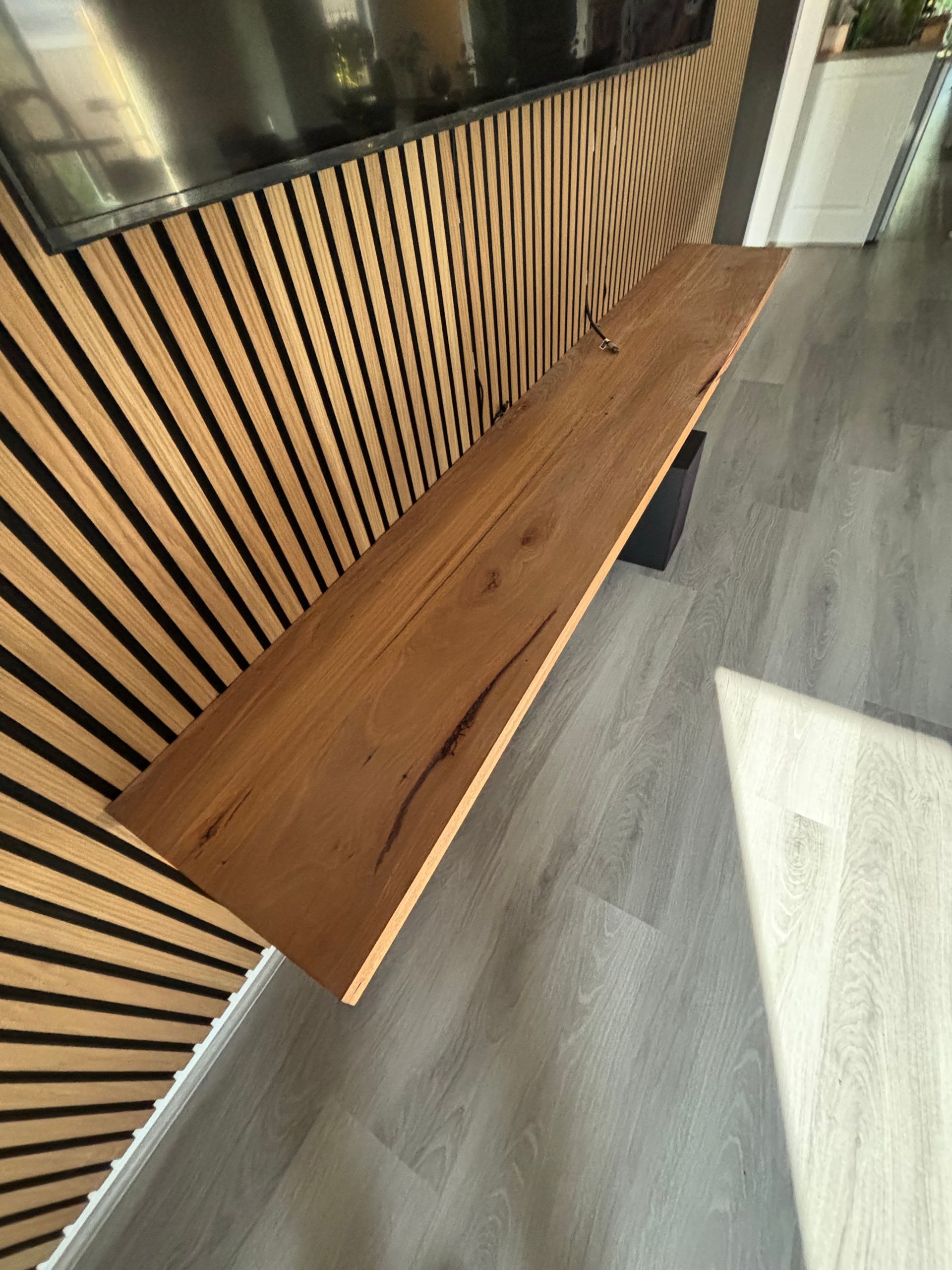 A wooden shelf is hanging on a wall next to a television.
