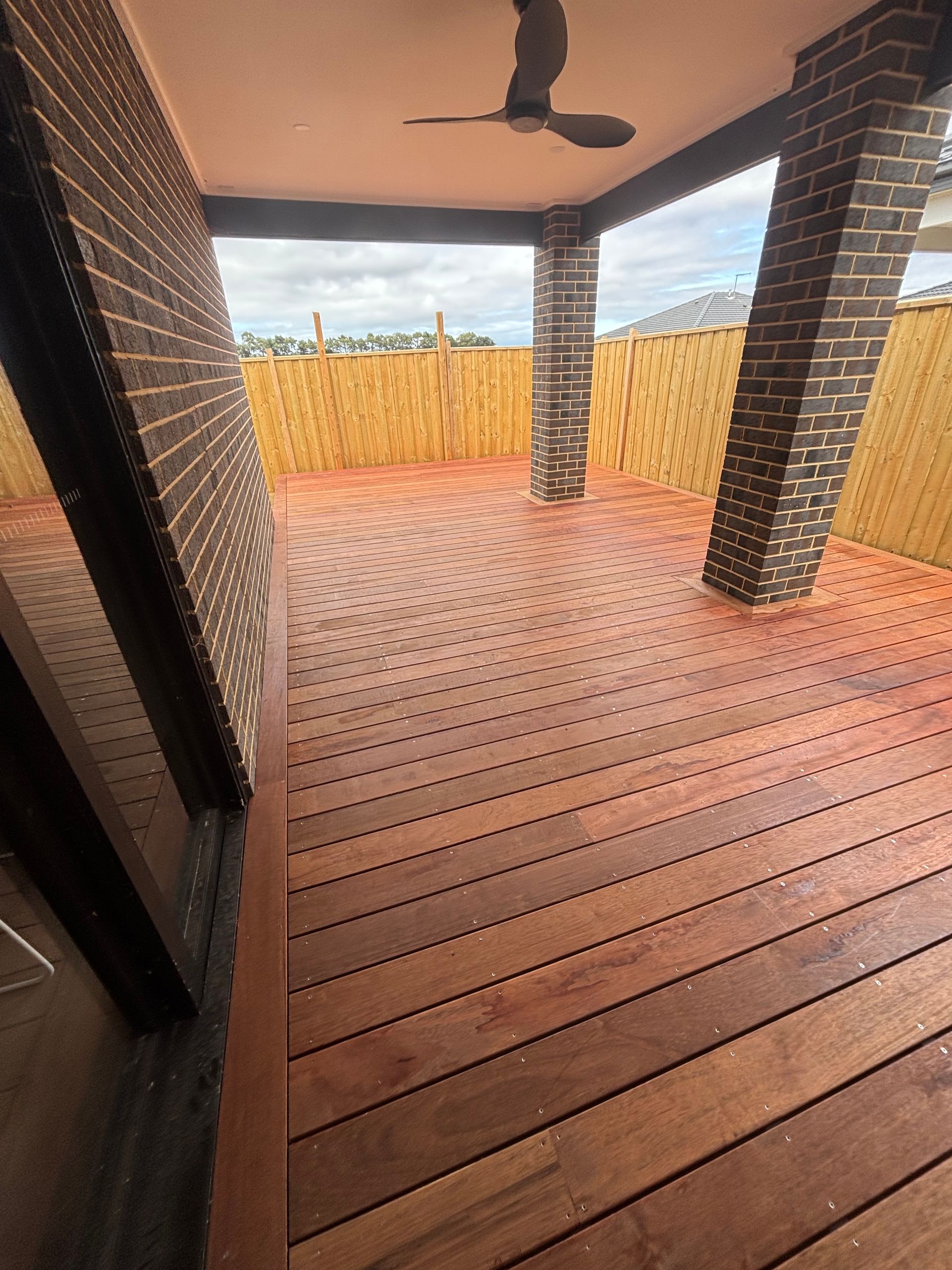 A wooden deck with a ceiling fan and a brick wall.