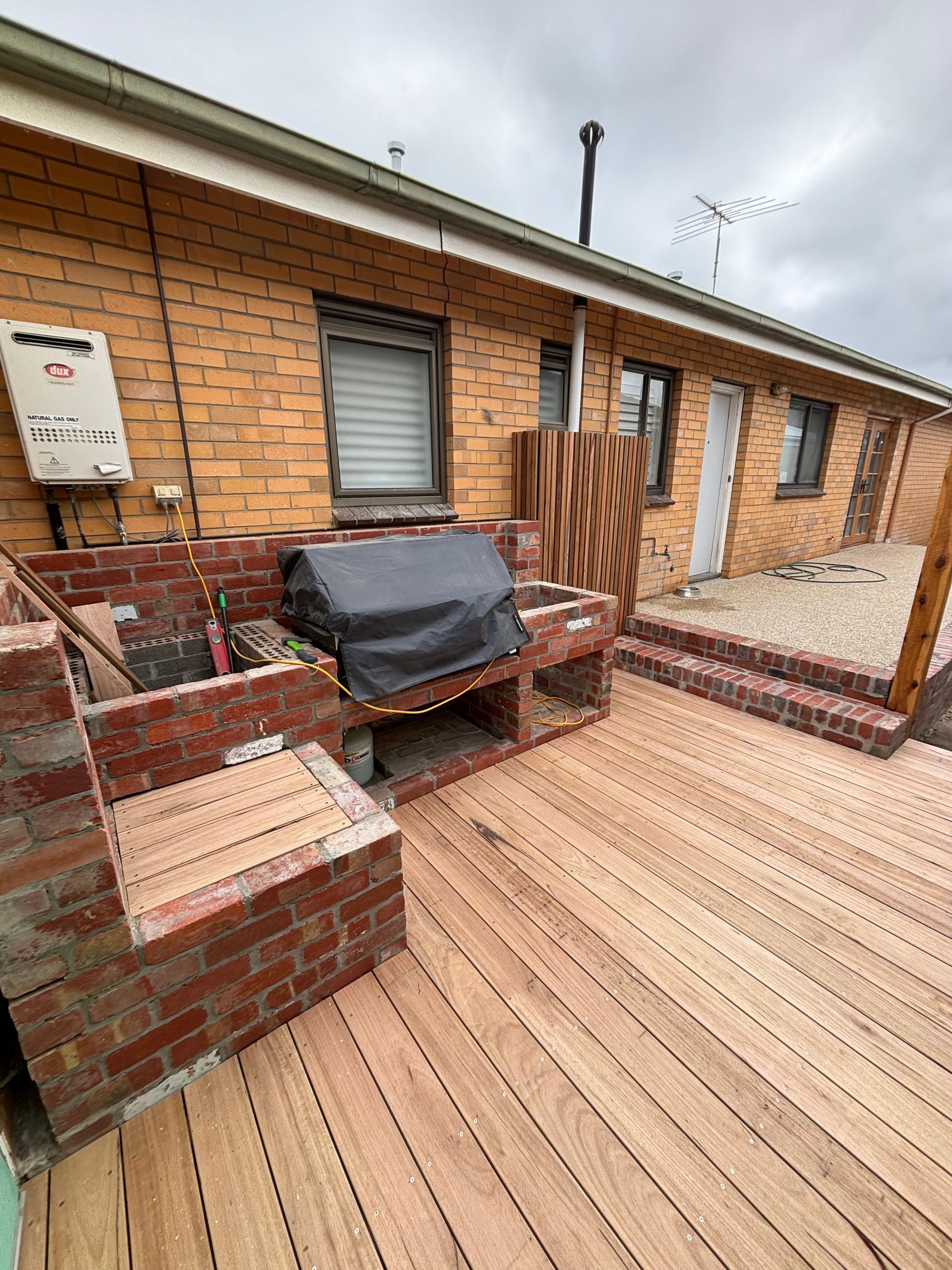 A wooden deck with a grill on it in front of a brick house.