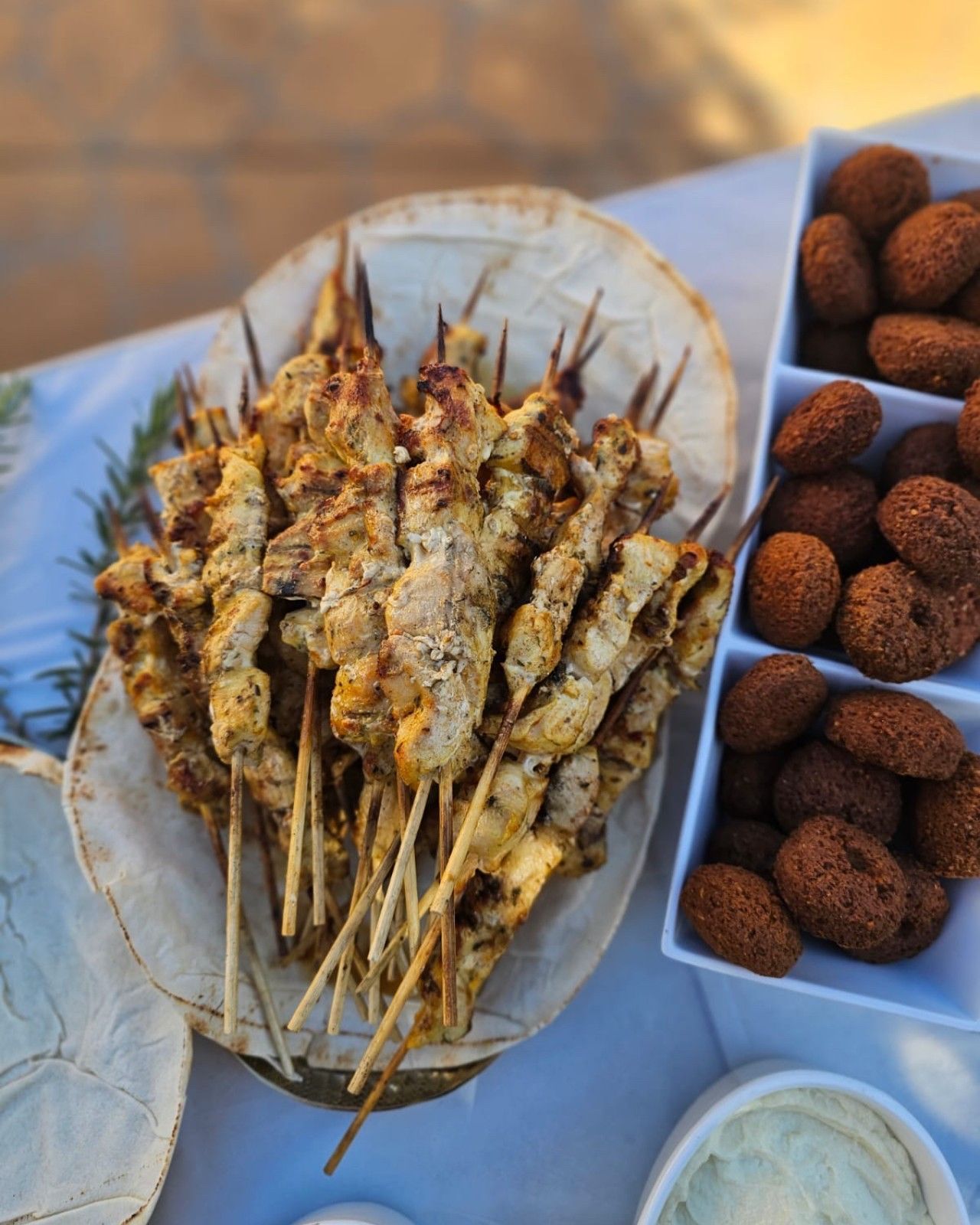 Grilled chicken skewers and falafel on a white table, outdoor setting. - The Habibiz Catering in Wingham NSW