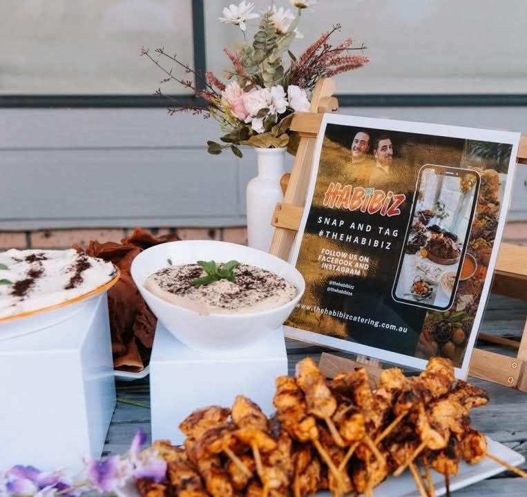 Table display with Middle Eastern food, flowers, and a sign. — The Habibiz Catering In Wingham, NSW