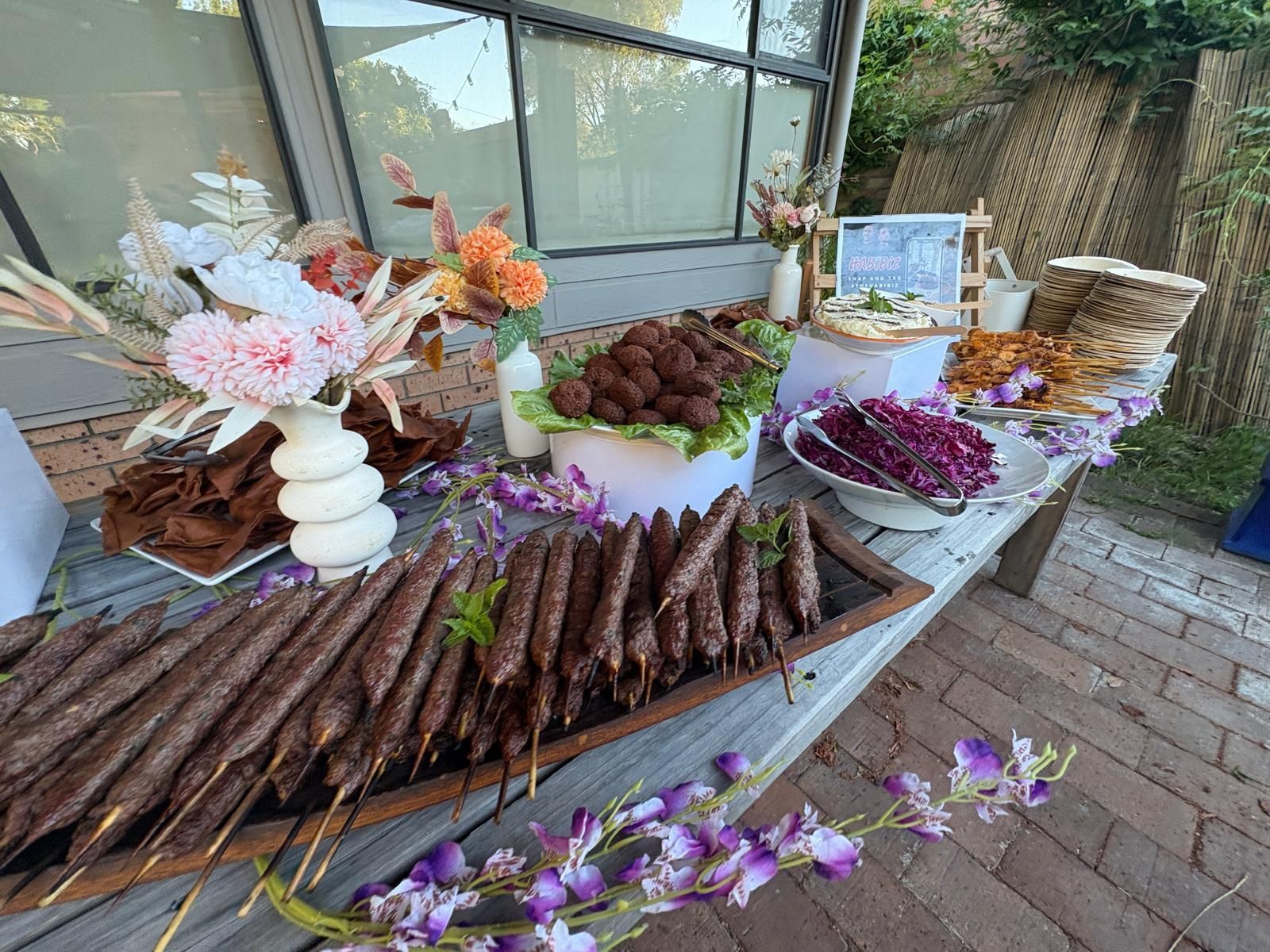 Catering table with skewers, meatballs, sides, and flowers. Outdoors, sunny setting. — The Habibiz Catering In Wingham, NSW