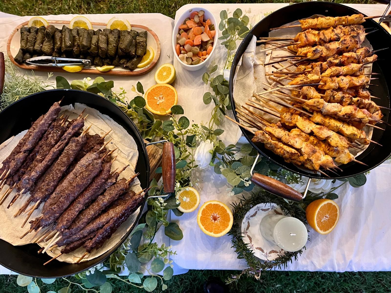 Outdoor spread with grilled meats on skewers, dolma, and dips, decorated with citrus and greenery. — The Habibiz Catering In Wingham, NSW