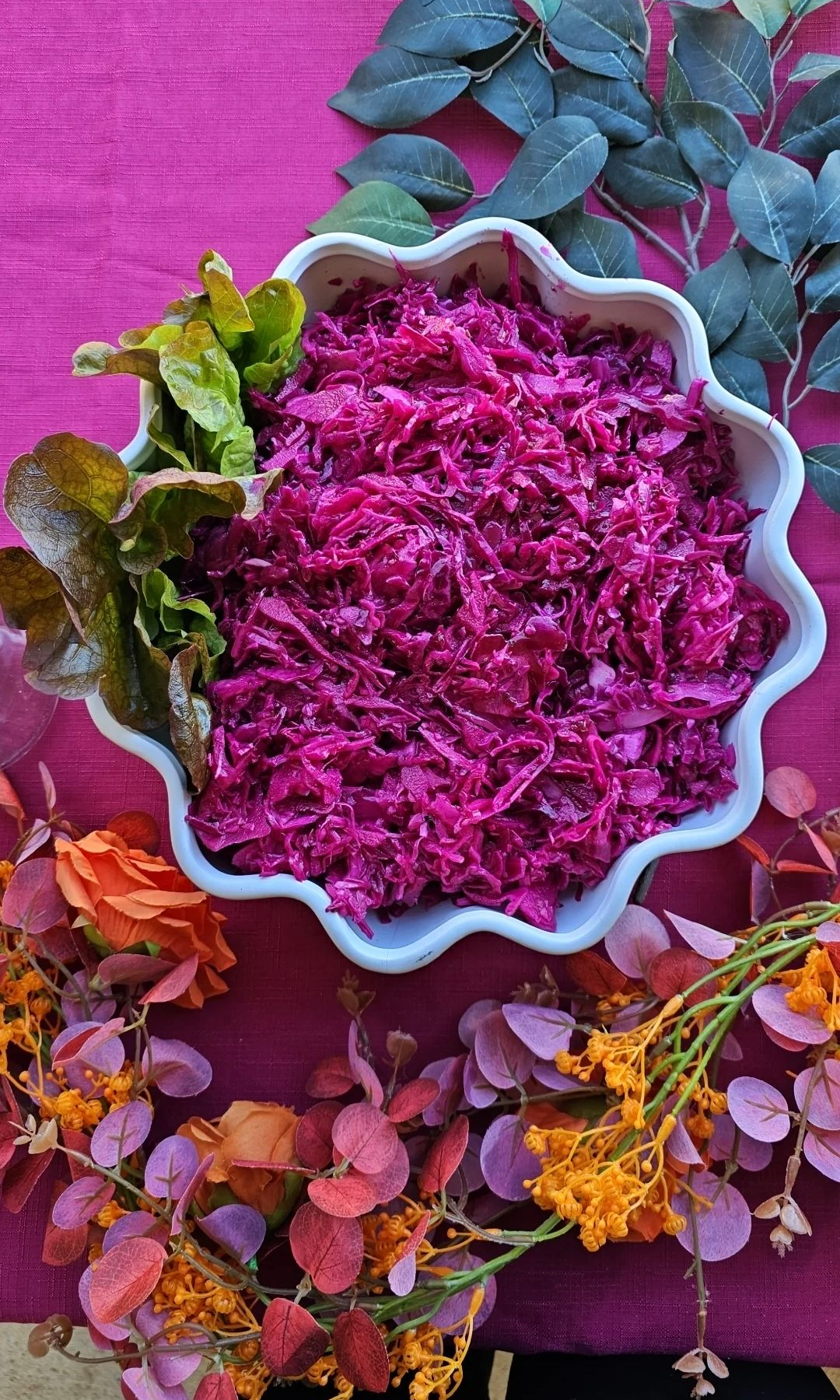 Purple cabbage salad in a white scalloped bowl, garnished with lettuce, on a fuchsia table with floral decorations. - The Habibiz Catering in Wingham NSW