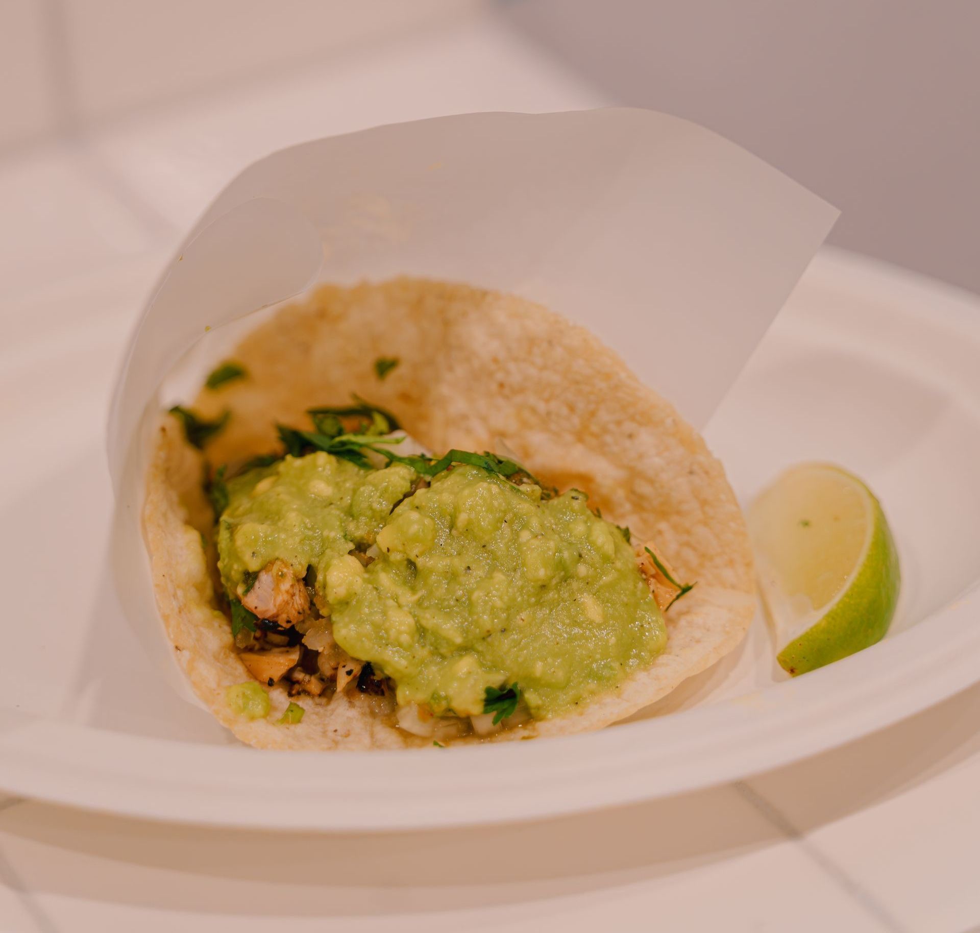 A taco with guacamole and a lime wedge on a paper plate.