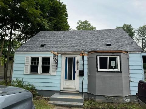 Small blue house with white trim, gray roof, front steps, and trees around it