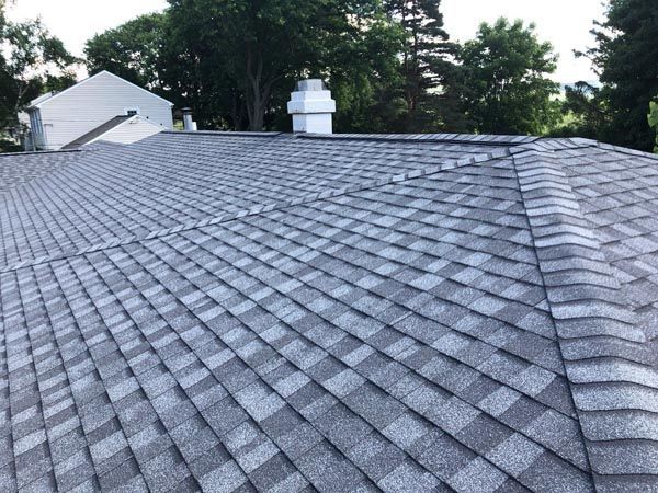 Gray shingle roof with a vent pipe, viewed from above against trees and a white house