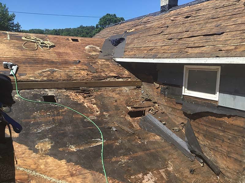 Rooftop under repair with peeled roofing, exposed wood, and a gray skylight against a blue sky