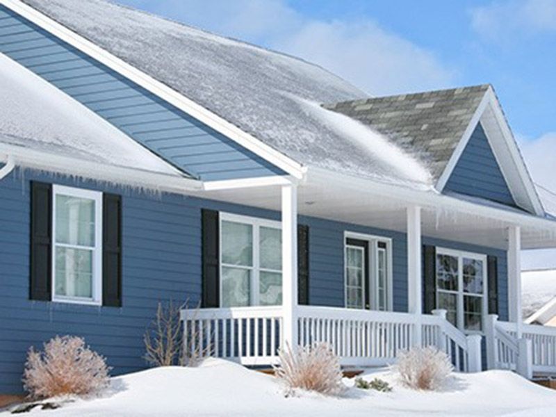 Snow-covered blue house with white porch and shutters in a winter neighborhood