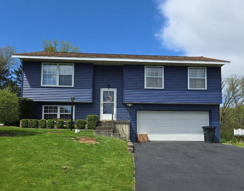 Blue split-level house with white garage door and front lawn on a sunny day