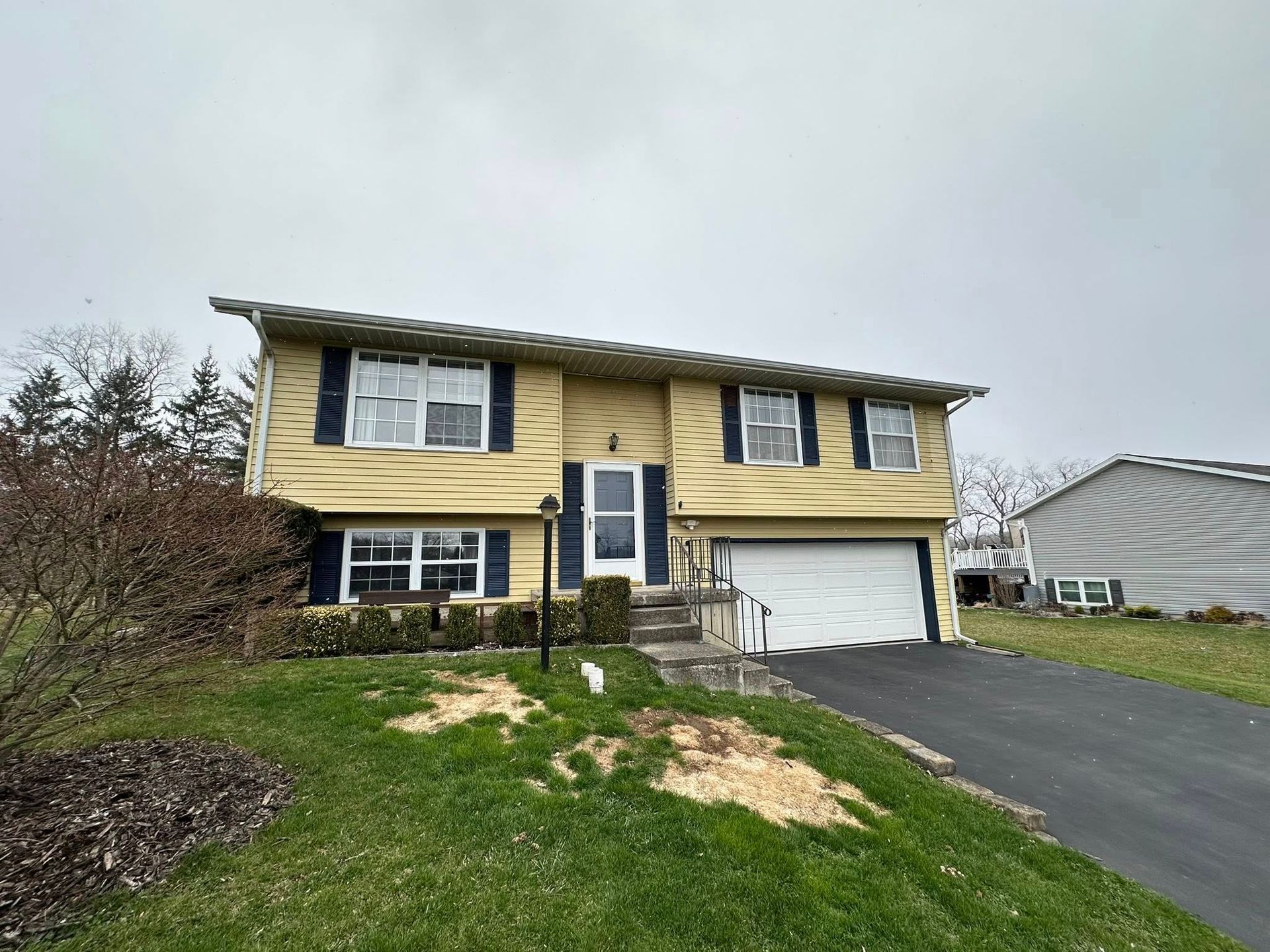 Suburban two-story yellow house with white trim, attached garage, driveway, and grassy front yard