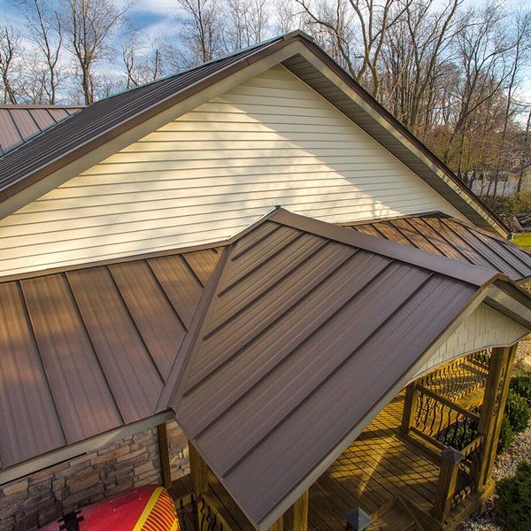 Brown metal roofs on a beige house with a covered porch and leafless trees in the background