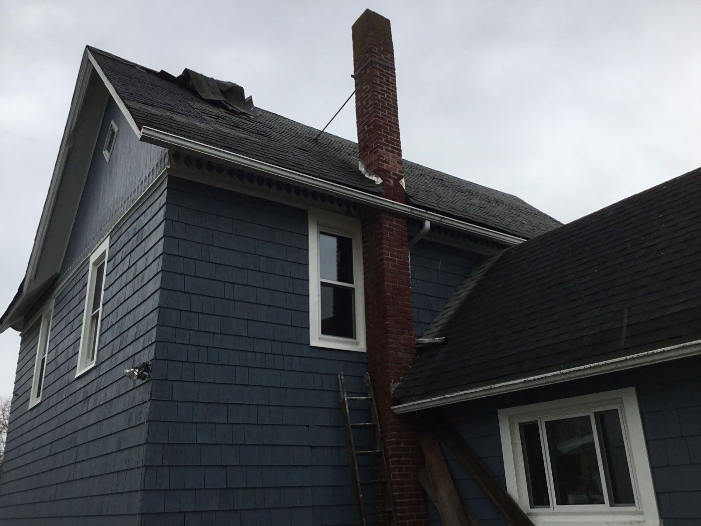 Blue-gray house exterior with a brick chimney and cloudy sky