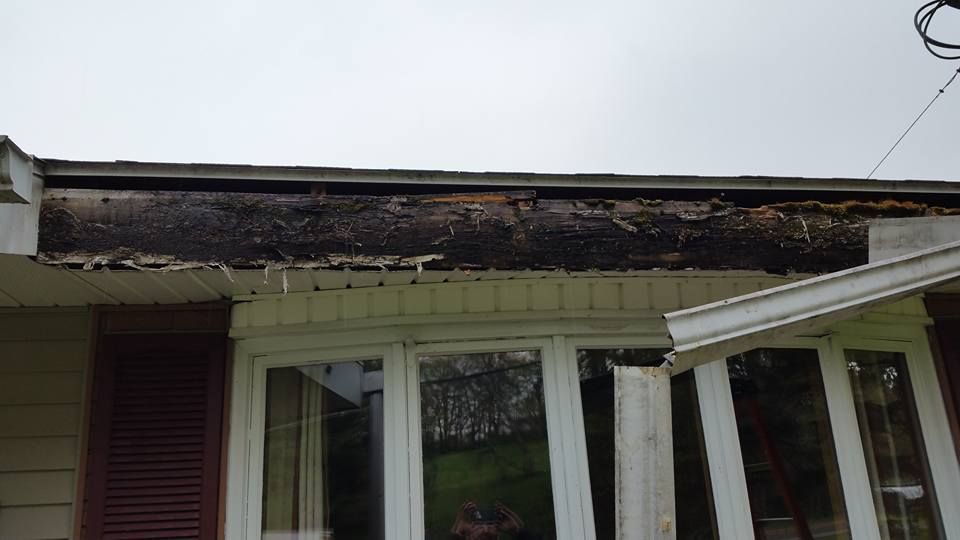 Damaged house roof with missing shingles and exposed rafters above a porch window