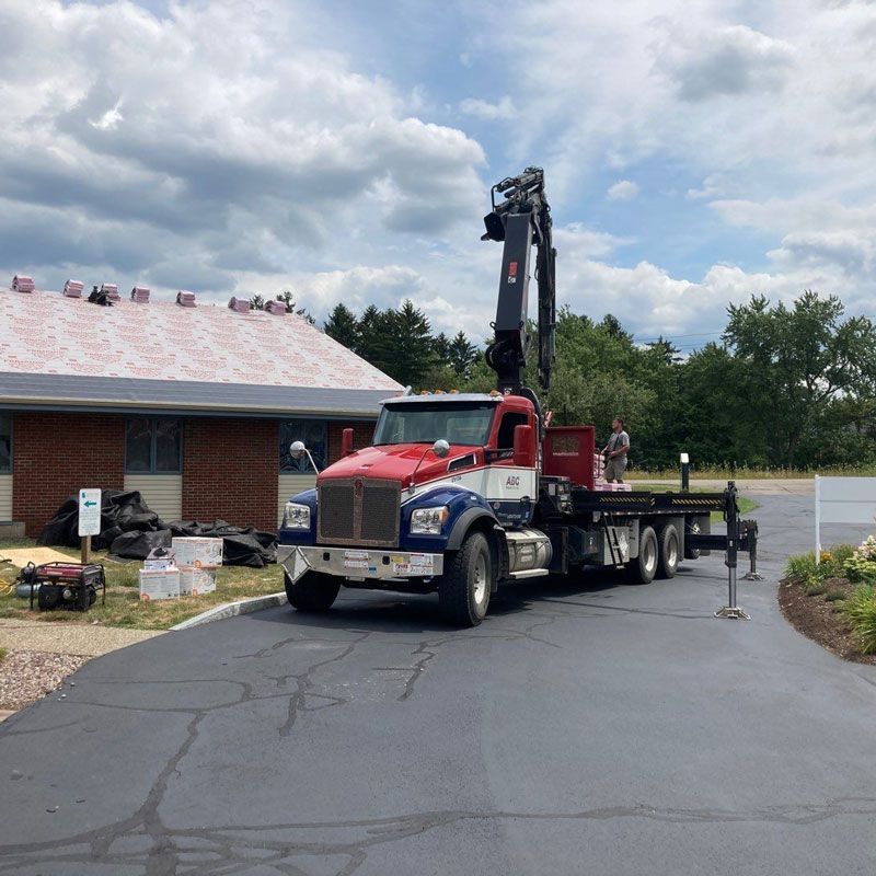 Red flatbed tow truck parked by a brick building, with a raised crane arm on a cracked parking lot.